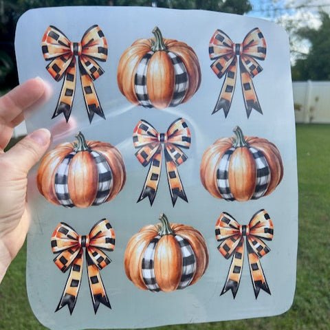 Sheet of decorative stickers with pumpkins and bows held over a grassy outdoor background