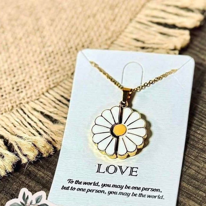 Gold necklace with a flower pendant on a card with text, placed on a textured surface.