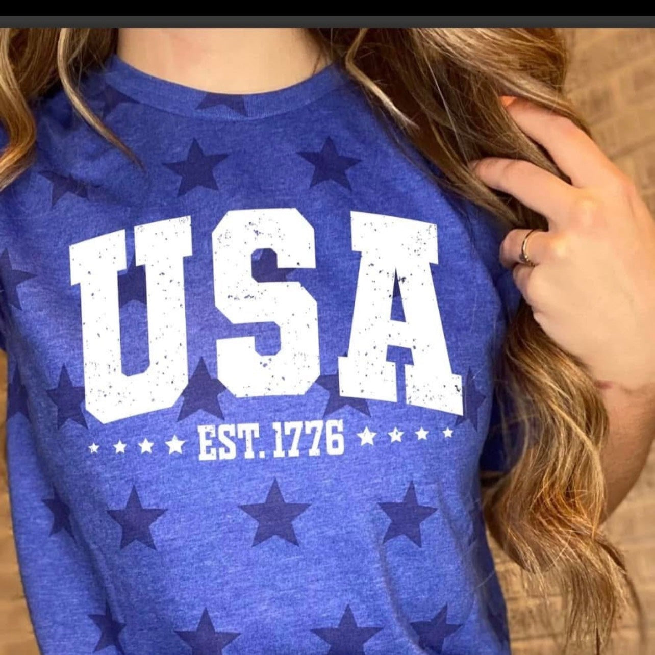 Blue t-shirt with 'USA EST. 1776' text and star patterns worn by a person.