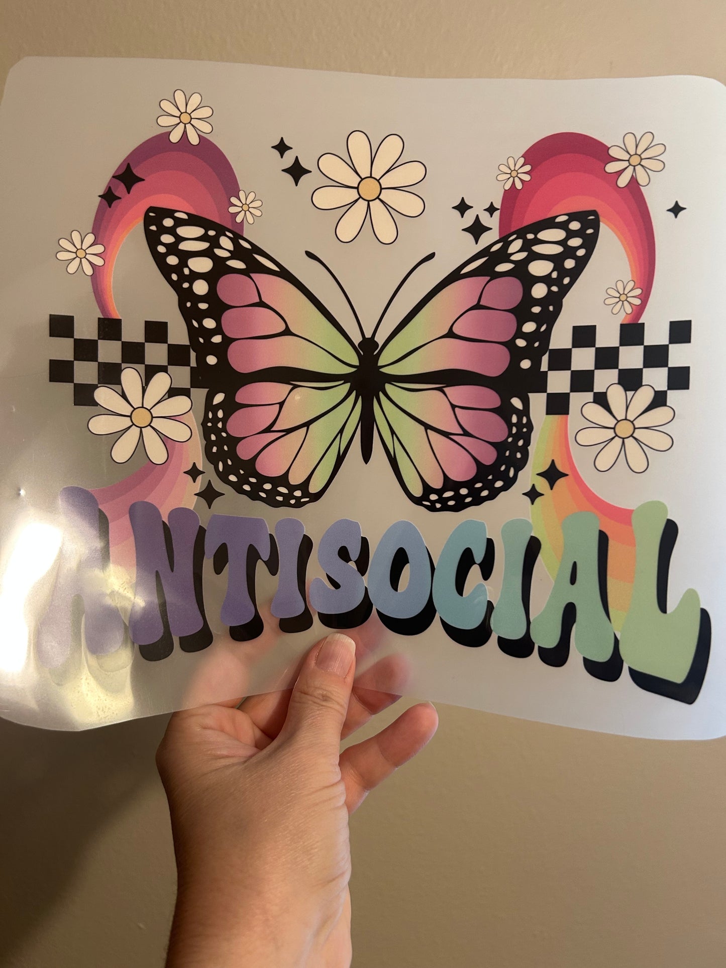 Hand holding a transparent sheet with a colorful butterfly design and the word 'MESOCALI'.