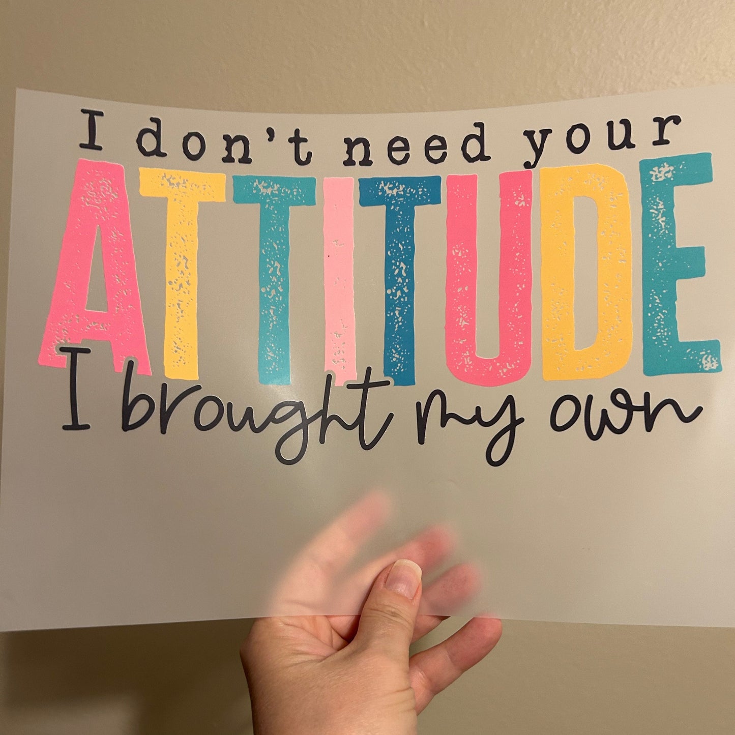Hand holding a sign with colorful text on a plain background