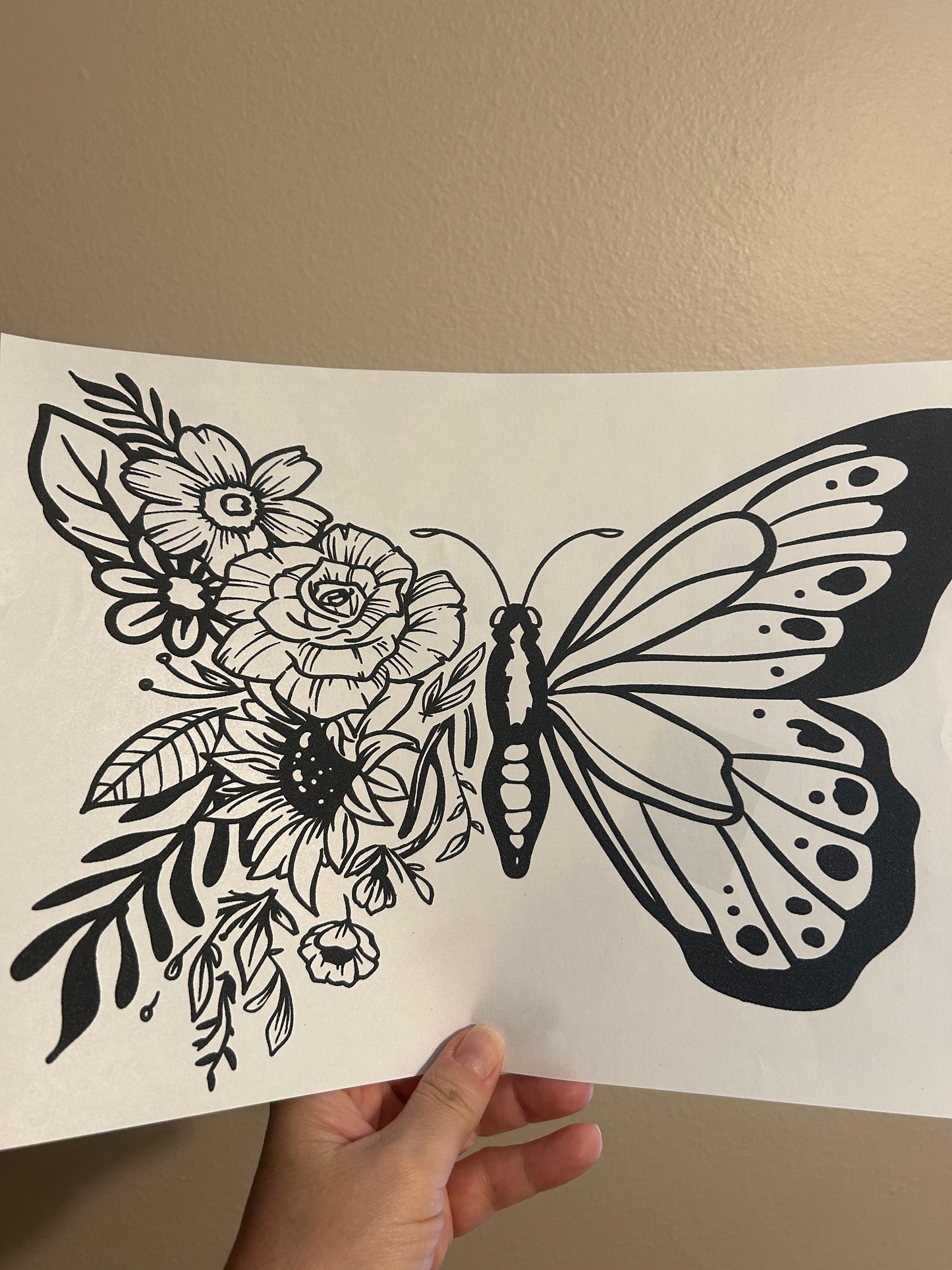 Hand holding a sheet of paper with a black and white butterfly and floral design.
