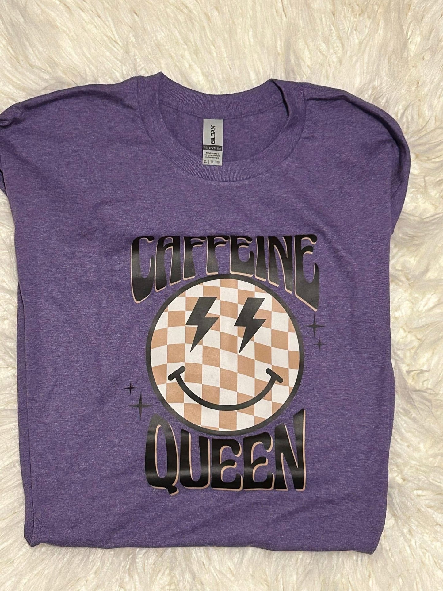 Purple t-shirt with 'Caffeine Queen' graphic design on a textured white background