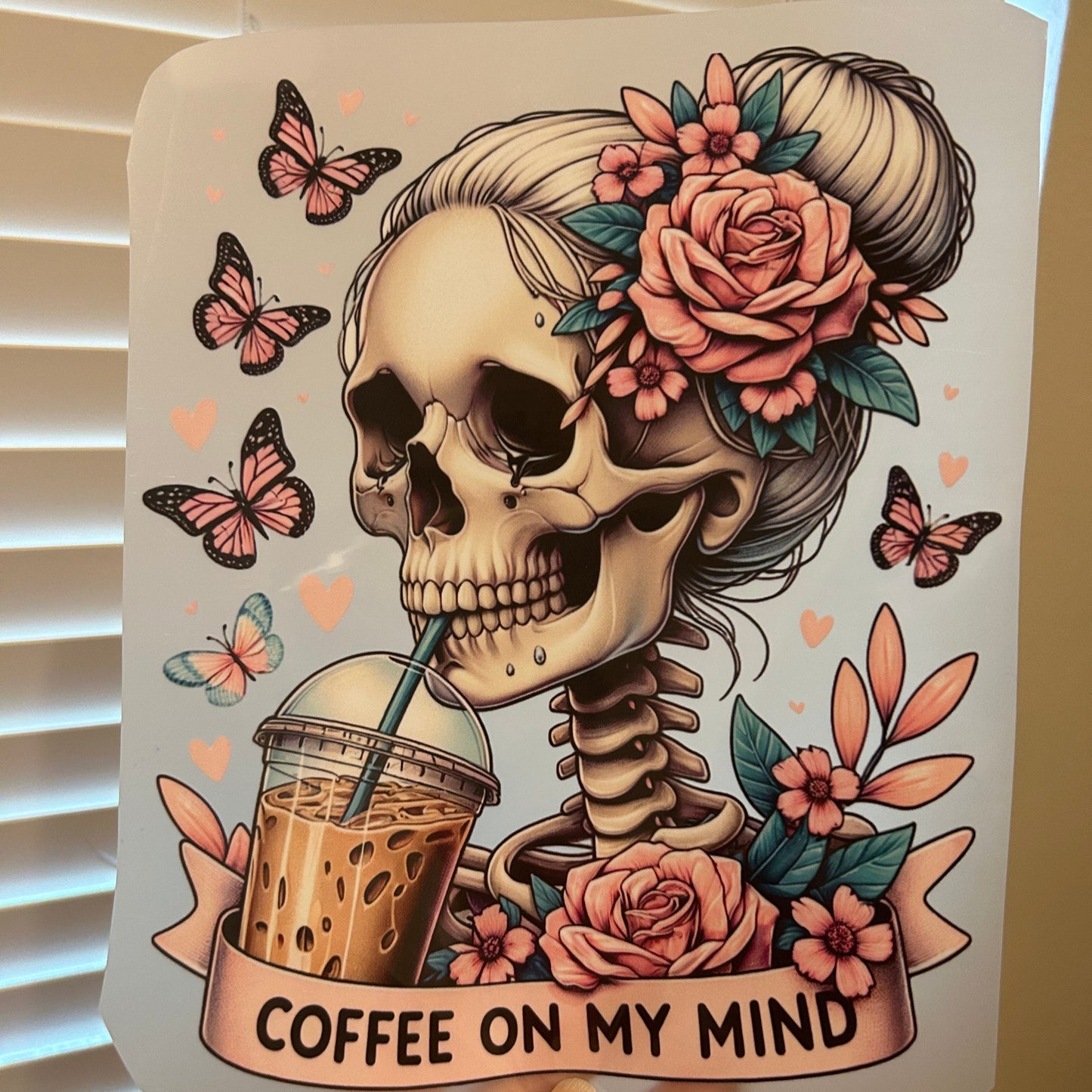 Decorative sticker with a skull, flowers, and 'Coffee on My Mind' text held by a hand.