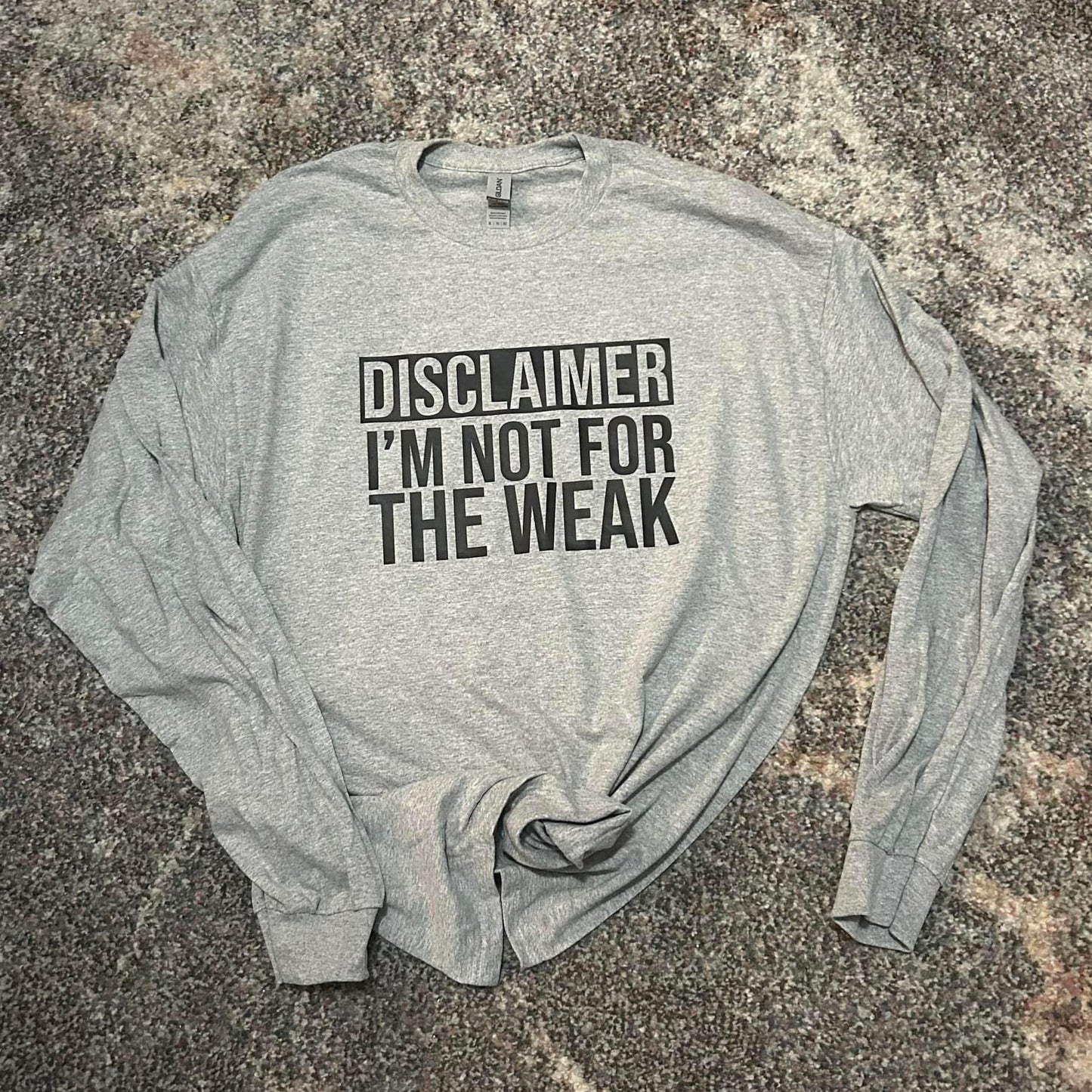 Gray long-sleeve shirt with text 'DISCLAIMER I'M NOT FOR THE WEAK' on a textured surface