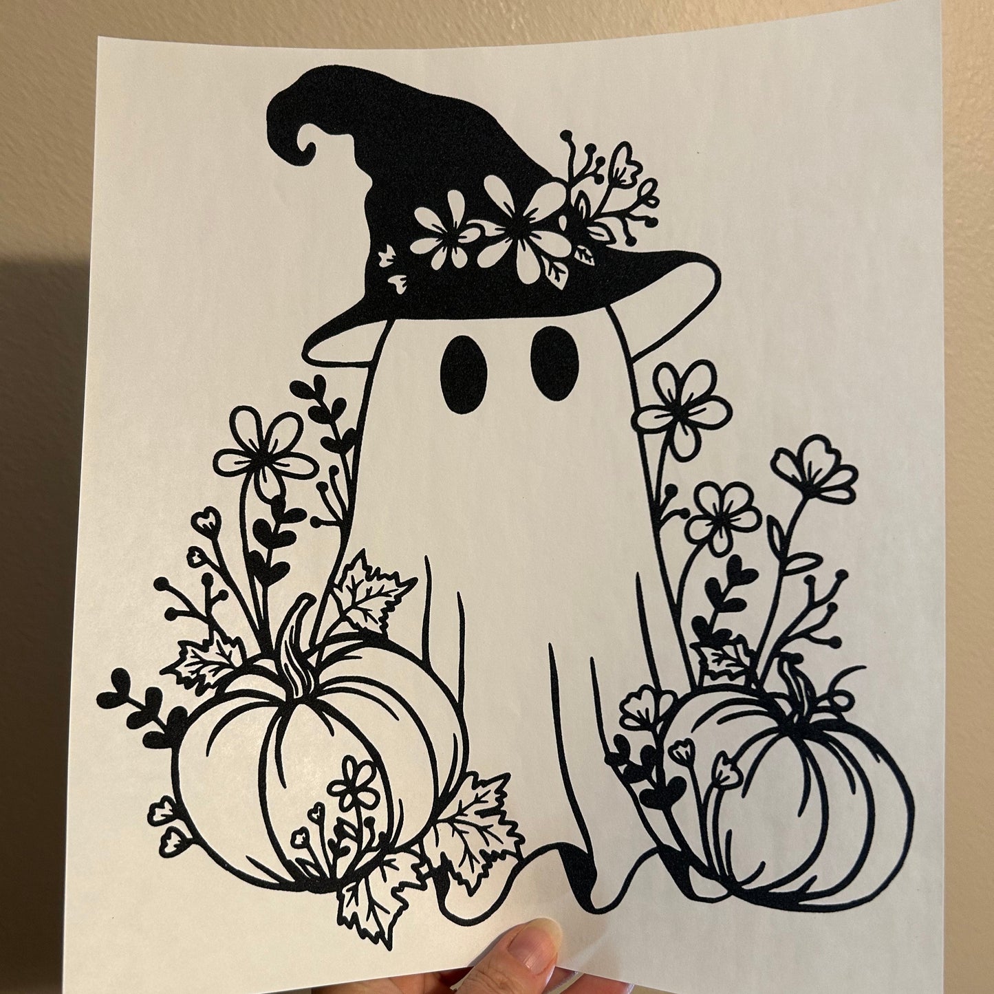 Decorative paper cutout of a snowman with floral elements held by a hand against a beige background.