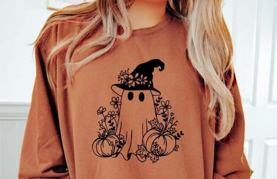 Person wearing a brown sweatshirt with a ghost and pumpkin design, featuring a witch hat.