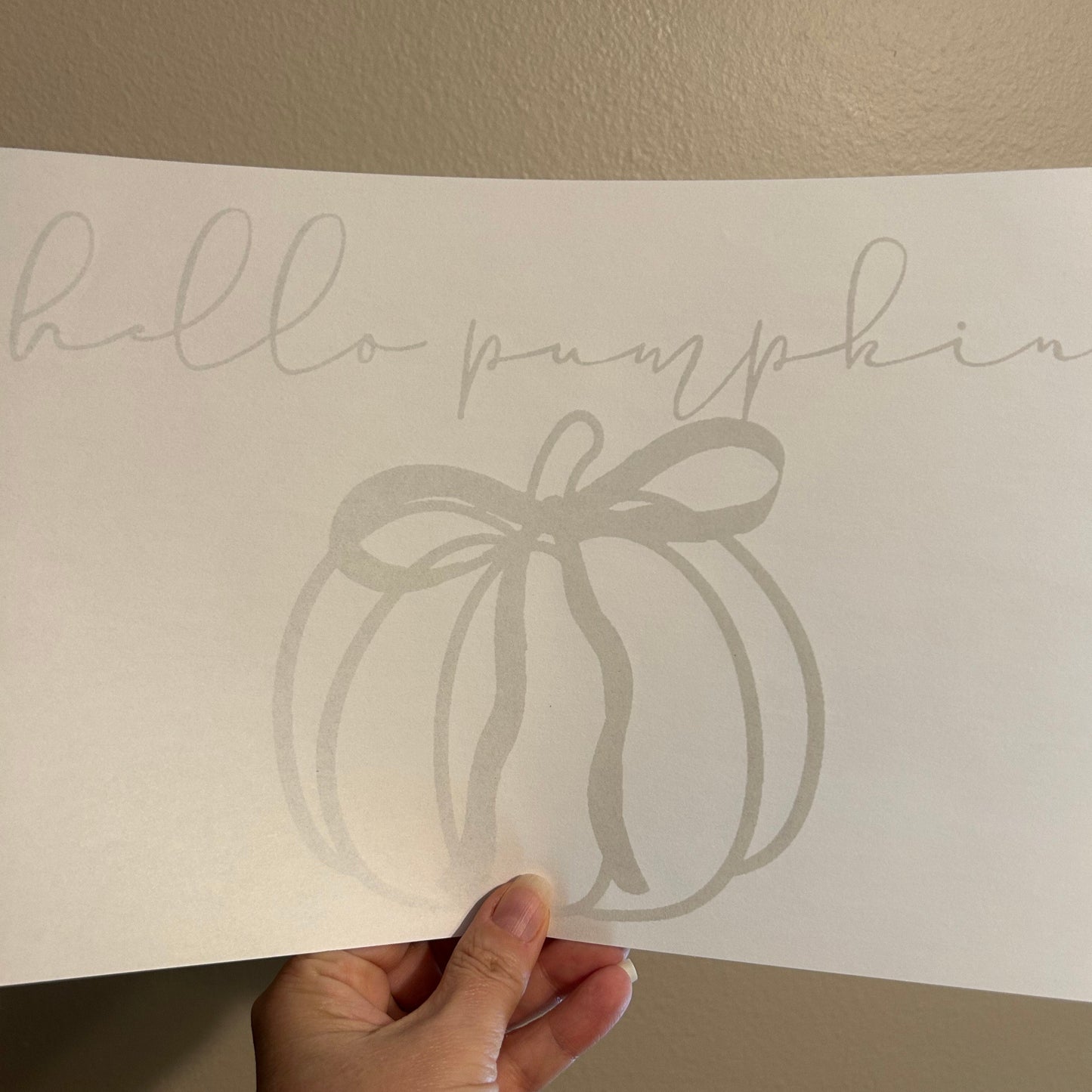 Sheet with pumpkin and text held by a hand against a beige wall