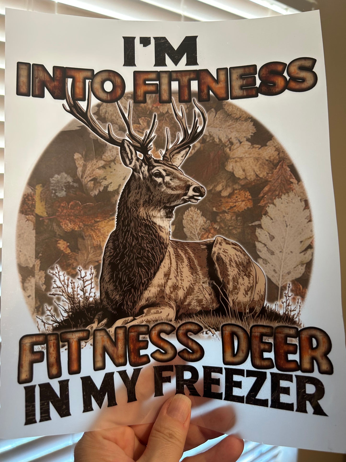 Hand holding a poster with a deer graphic and text about fitness and hunting.