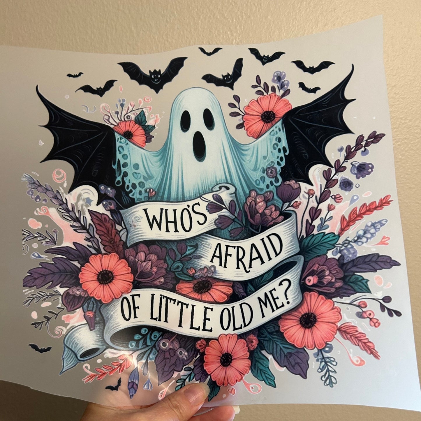 Decorative paper with ghost, flowers, and text held by a hand against a beige background