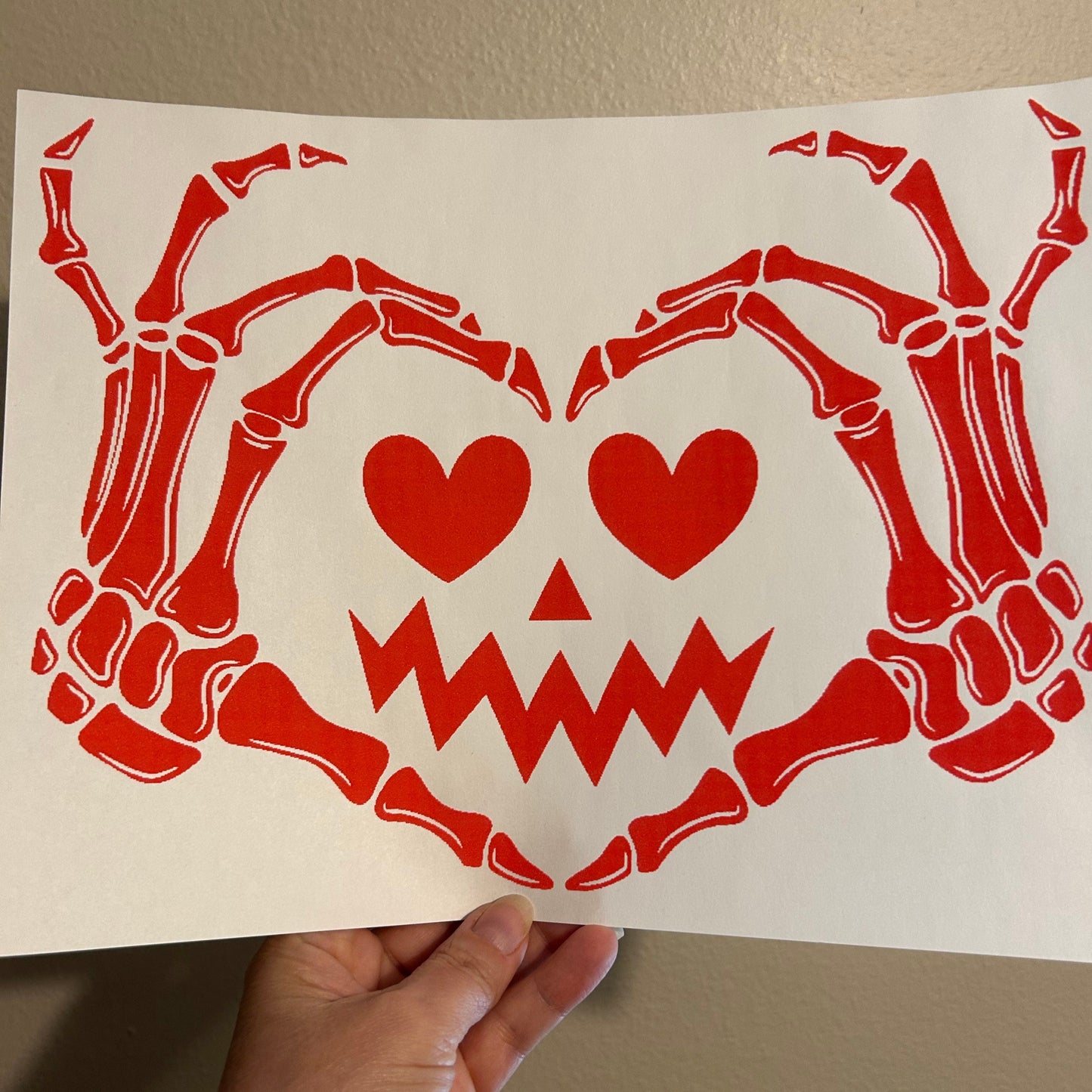 Red skeleton and heart design on a white card held by a hand against a beige background