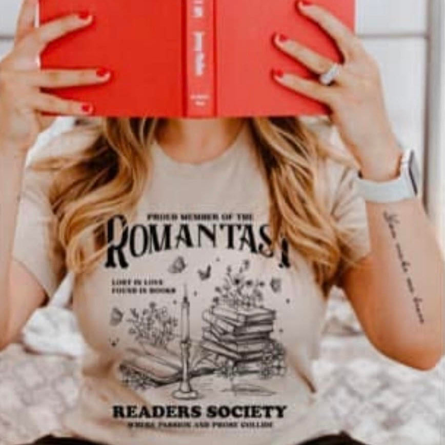 Person wearing a t-shirt with 'Romantic Readers Society' text, holding a red book.