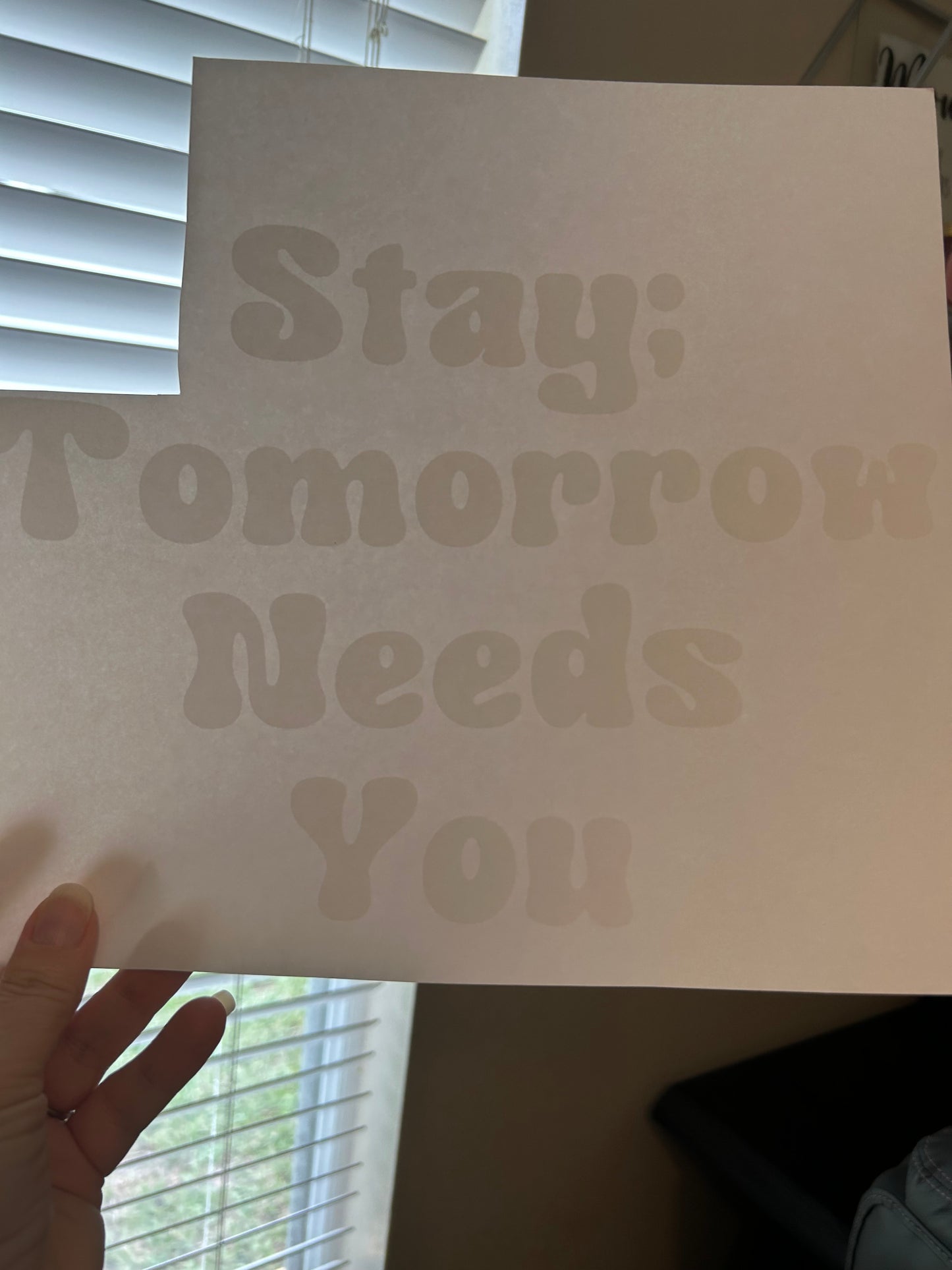 Sheet of paper with text 'Yesterday Needs You' held by a hand in front of blinds.