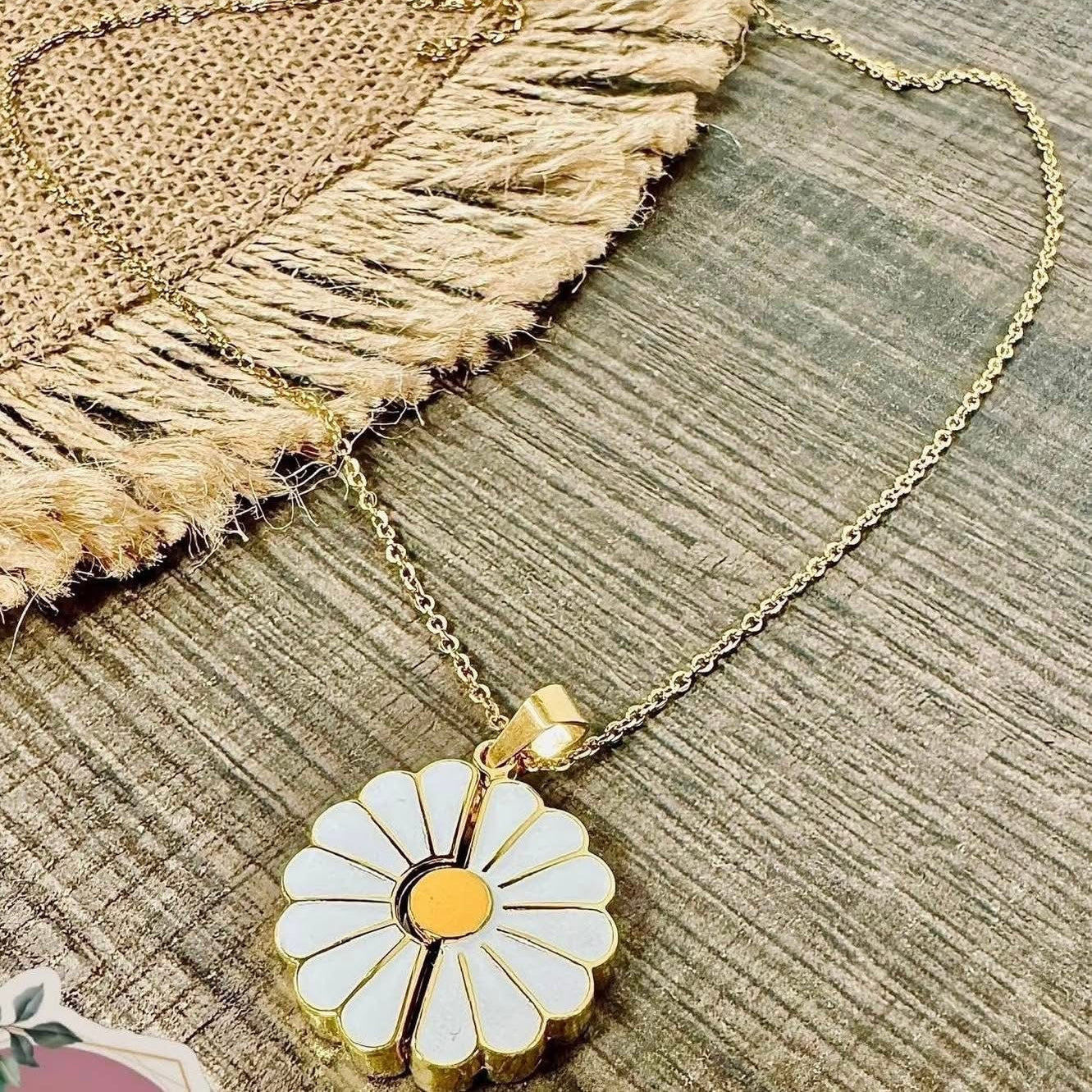 Gold necklace with a white flower pendant on a textured surface