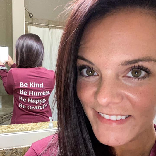 Woman wearing a maroon shirt with motivational text, standing in front of a mirror.