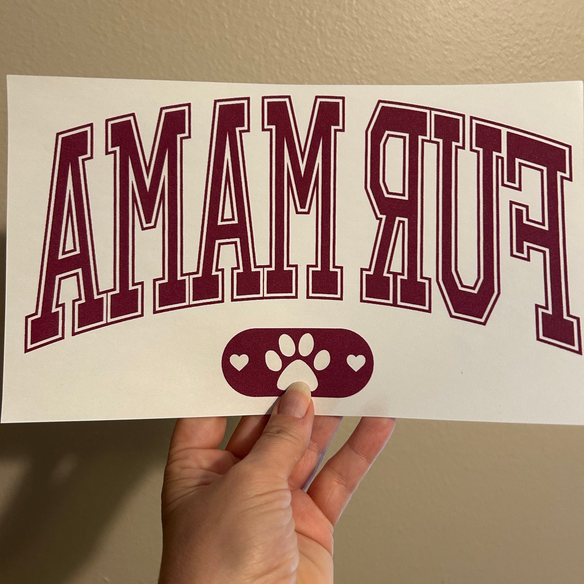 Hand holding a decal with 'AMAWY' text and paw print design on a beige background