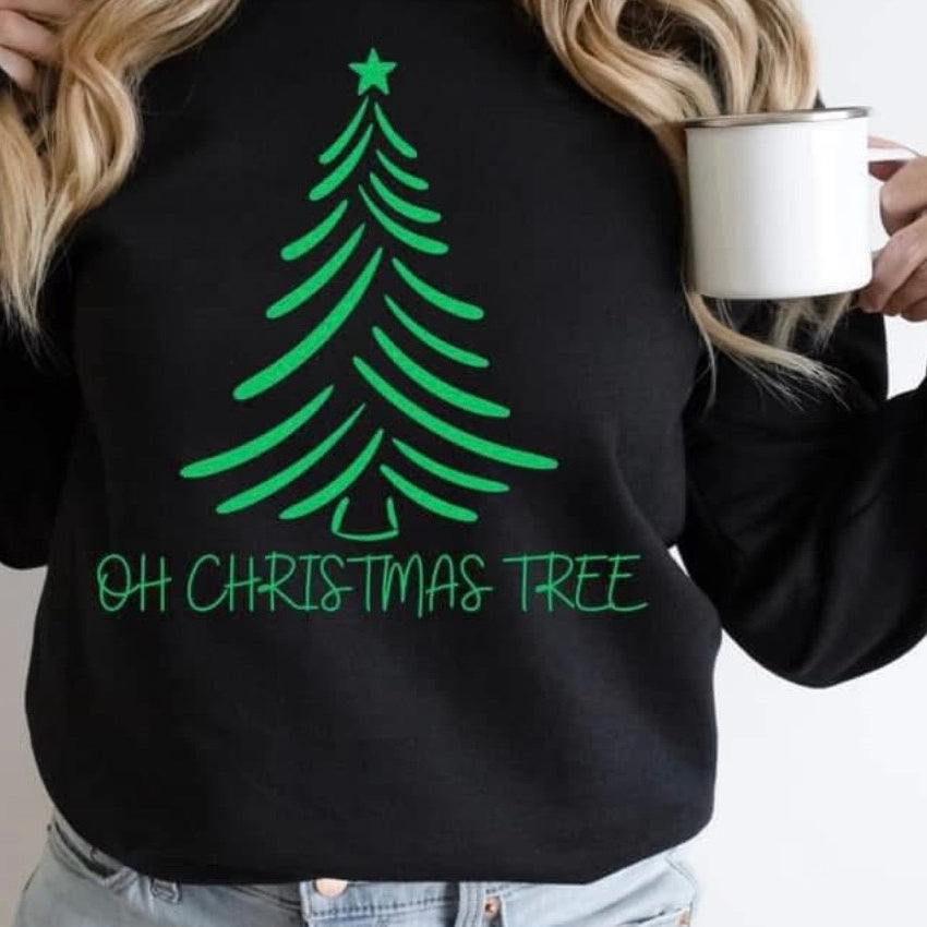 Black sweatshirt with green Christmas tree design and text, worn by a person holding a mug.